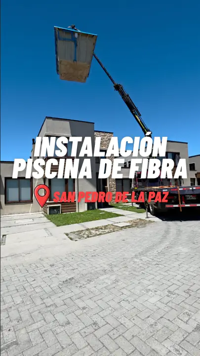 Grúa sosteniendo en el aire el casco de una piscina de fibra frente a la casa